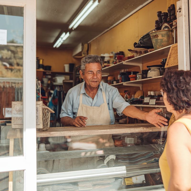 Dono de pequeno comércio brasileiro atendendo cliente no balcão